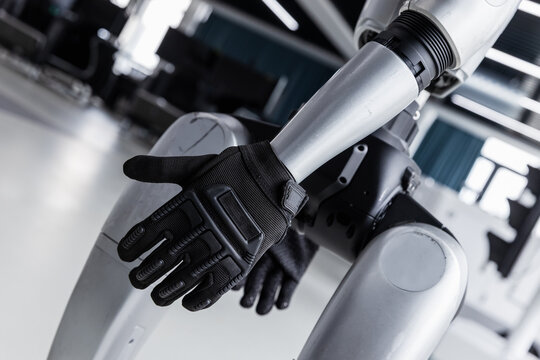 Futuristic robotic arms fitted with black tactical gloves sit in a modern technology lab, highlighting advanced robotics, protective gear integration, humanoid design and automation in engineering