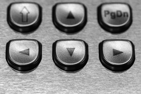 Close-up black and white photo of metal navigation buttons with directional arrow symbols and a PgDn key on a brushed stainless control panel, conveying technology, precision, and interface design