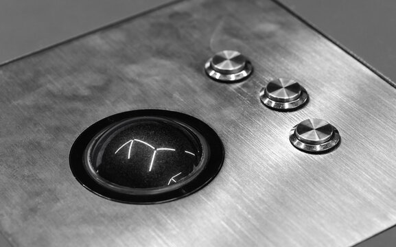 Close-up monochrome shot of a trackball navigation control integrated into a brushed stainless steel panel with three metal push buttons, evoking retro industrial design and tactile interface