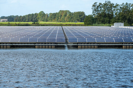 View of floating solar panels installed on a calm lake with lush green trees in the background in Beilen, Drenthe, Netherlands.