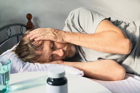 Man having severe headache in bed with medication and water on nightstand