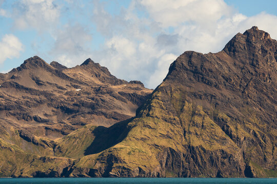 View of Jason Harbour with rugged mountain peaks and rocky coastline under a cloudy sky in South Georgia and the South Sandwich Islands.