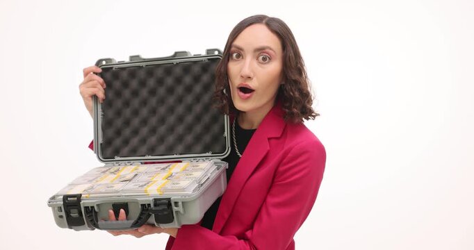 Exited businesswoman in pink blazer holds open briefcase with dollar banknotes on white background. Lady entrepreneur shocked by unexpected profit