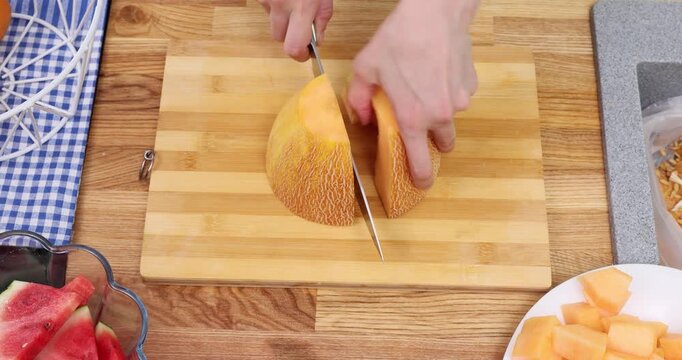 Woman hands pour fruit dice onto plate and slice juicy melon on table upper view. Female serves delicious natural summer dessert in kitchen timelapse