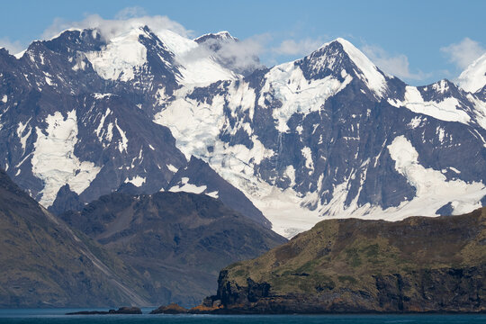 View of the rugged, snow-capped mountains and glaciers rising above the rocky coastline in Grytviken, South Georgia and the South Sandwich Islands.