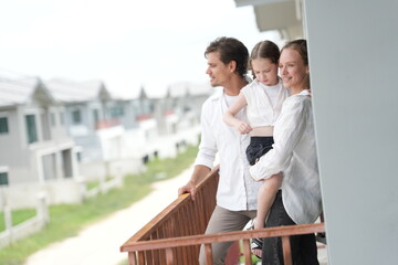 Obraz premium Caucasian family of three embracing stand at the wooden railing admiring the neighborhood view on the upper balcony of their new home above the neighborhood, authentic everyday scene