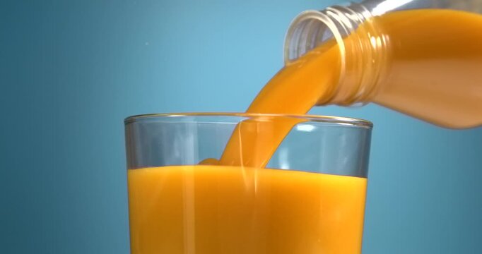 Orange juice pouring from bottle into glass in slow motion on blue background