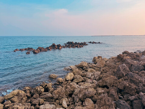 View of a rocky shoreline with jagged stones along the coast and calm sea water under a soft twilight sky in Indonesia.
