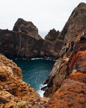 View of the rugged volcanic cliffs and deep blue Atlantic Ocean at Ponta de Sao Lourenco with a hiker standing on the rocky trail in Canical, Madeira, Portugal.