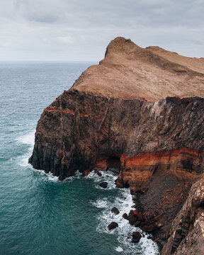 View of the rugged volcanic cliffs of Ponta de Sao Lourenco meeting the Atlantic Ocean with layered rock formations and crashing waves in Canical, Madeira, Portugal.