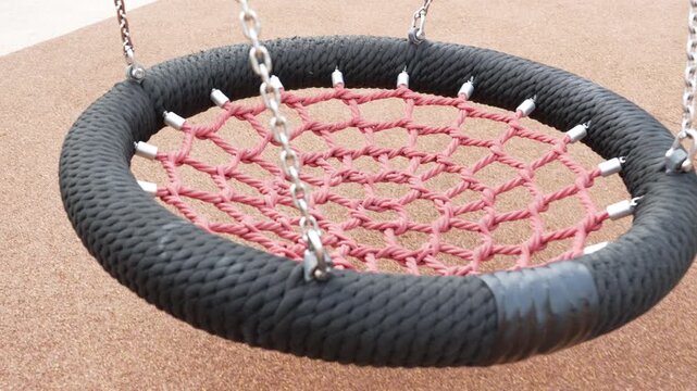 Empty modern nest swing with a heavy black woven rope border on a playground.