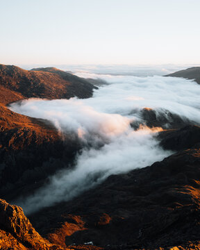View of Crib Goch mountain ridge with thick clouds filling the valley during golden hour in Caernarfon, Wales, United Kingdom.