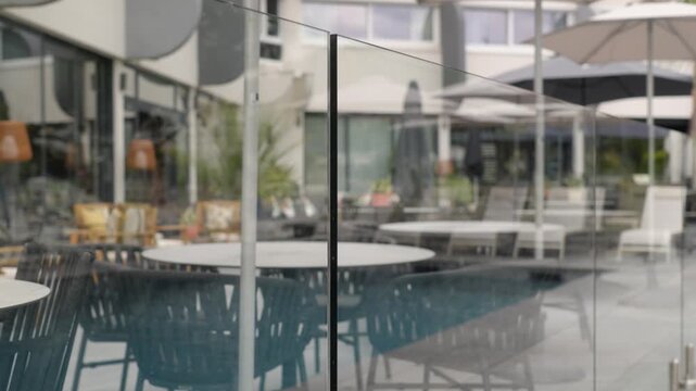 Glass safety fence borders a modern outdoor pool and furnished hospitality terrace with umbrellas