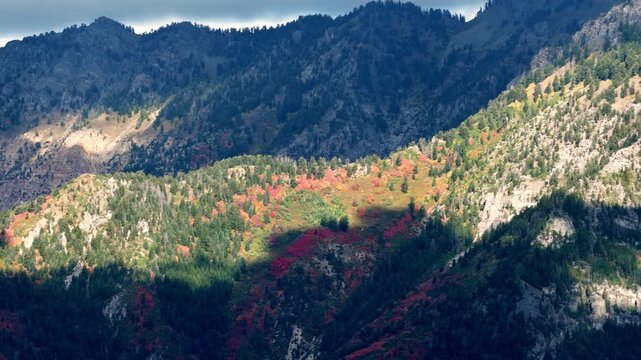 Stunning time-lapse of autumn mountainside bathed in shifting cloud shadows, showcasing vivid fall foliage, dynamic light patterns, and dramatic natural scenery in a static wide shot.