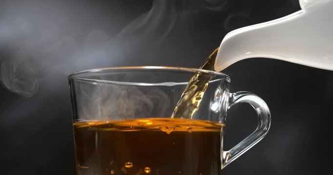 Tea pouring from teapot into transparent mug in slow motion