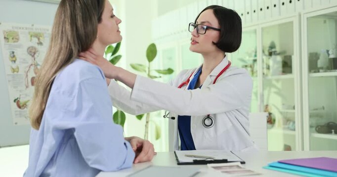 Female doctor examines neck during clinical checkup. Physician palpates throat area checking thyroid region while female patient remains seated