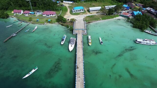 Aerial drone view of Teluk Sulaiman pier in Biduk Biduk Berau East Kalimantan Indonesia with boats anchored in turquoise clear water and lush Borneo forest