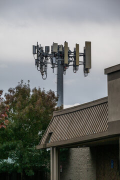 View of a tall metal cell tower with multiple antennas and equipment against a cloudy sky, rising above a building roof in Portland, Oregon, United States.