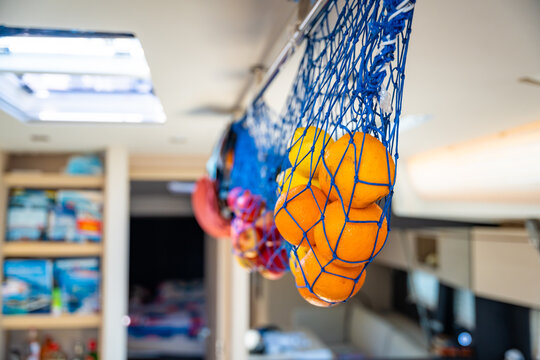 Fresh oranges and other citrus fruits stored in a hanging net inside a yacht galley during a sailing trip. Concept of healthy nutrition, vitamin supply, food storage, self-sufficient cruising