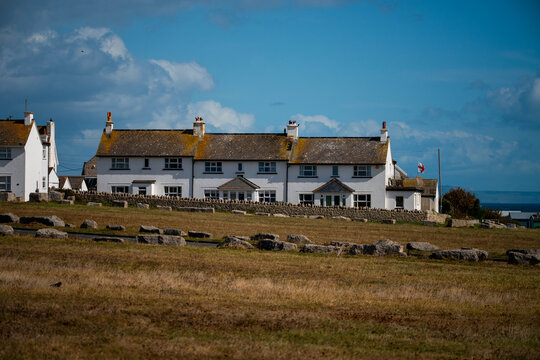 View of the Isle of Portland featuring a row of traditional white houses with stone walls and a grassy field under a blue sky in Portland, England, United Kingdom.