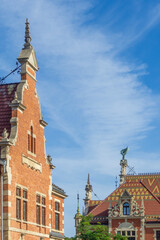 Ornate red brick architecture of Gdańsk Główny Railway Station under a clear blue sky, featuring intricate gables, roof tiles, and decorative elements © photoopus