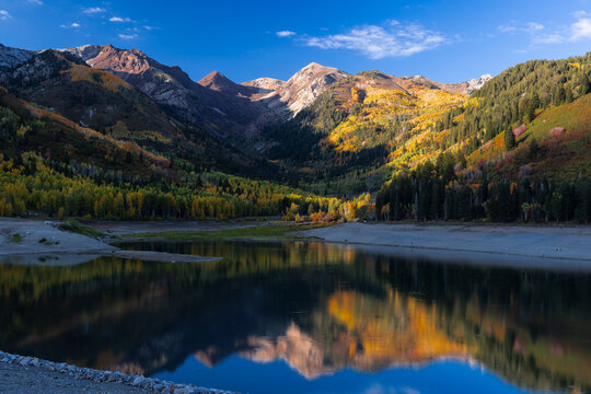 View of Silver Lake Flat Reservoir reflecting the surrounding mountains and autumn foliage under a clear blue sky in Utah County, Utah, United States.