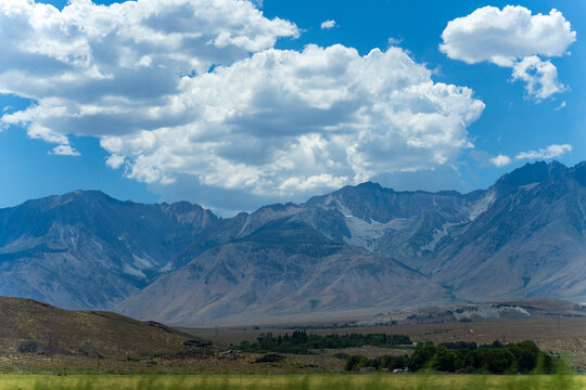 View of the rugged Eastern Sierra mountains rising above the arid landscape under a bright blue sky with large white clouds in Independence, California, United States.