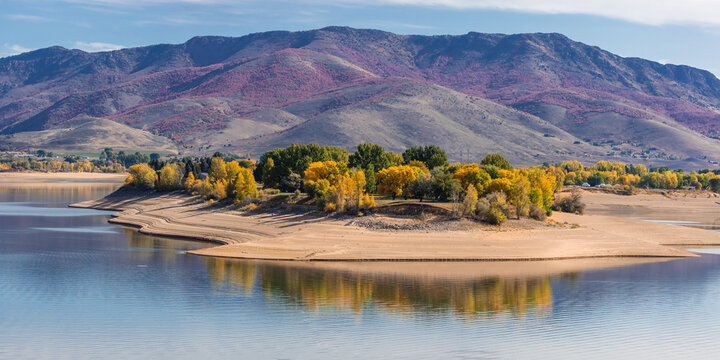 View of autumn foliage on the shores of Pineview Reservoir with the Wasatch Mountains in the background in Ogden, Utah, United States.