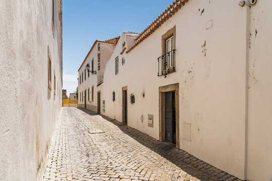 View of a narrow cobblestone street lined with traditional white buildings in the historic center of Faro, Faro District, Portugal.