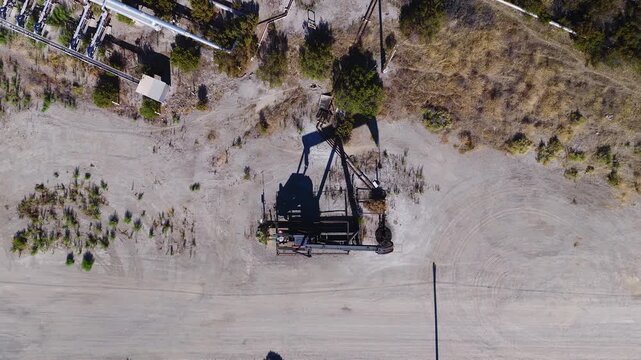 Aerial top down perspective shows an operating oil pump jack working on arid ground in California, USA. Oil tariffs, trade war, price plunge.