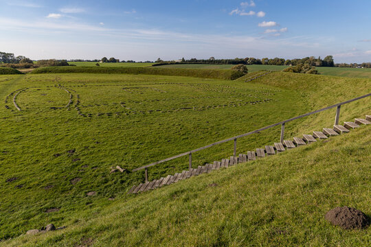View of The Viking Fortress Trelleborg, showing the circular earthen ramparts and stone outlines of longhouses on a grassy field under a clear blue sky in Slagelse, Sjaeland, Denmark.