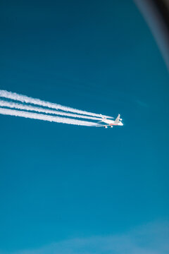 View of a commercial passenger airplane flying high in the sky leaving long white contrails against a clear blue sky over Oslo, Oslo, Norway.