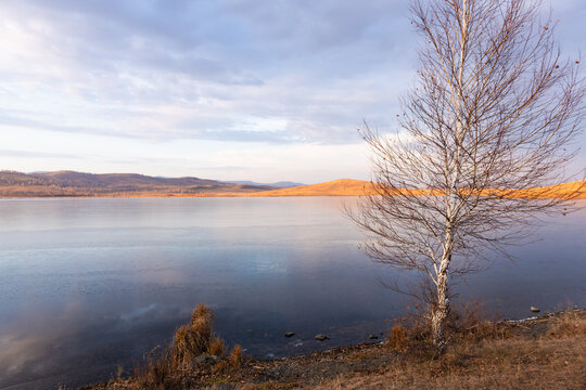Ice on the lake at sunset. Yellow autumn trees and mountains on the shore of lake. Beautiful autumn landscape.