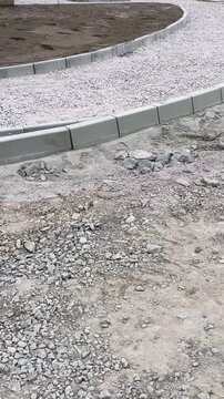 Curved concrete curbstones set beside gravel pathway, with loose crushed rock and compacted soil showing paving and landscaping fine details. Curved concrete curb, paving progress