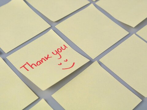 Close up of a yellow adhesive note with a handwritten Thank you message and happy face in red ink, surrounded by blankadhesive notes on a flat surface. Perfect for business and gratitude concepts