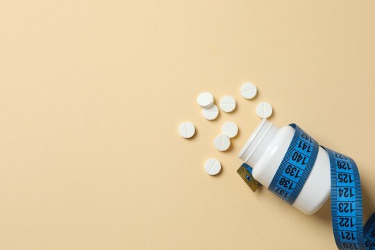 White jar of weight loss pills and blue measuring tape on color background