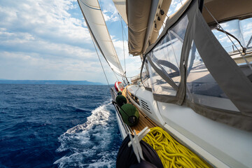 Obraz premium Dynamic view from deck of sailing yacht heeling under wind power while cutting through Adriatic waters. White wake, filled sails, a sense of speed, freedom and offshore adventure