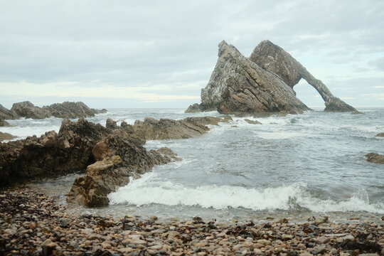 View of Bow Fiddle Rock with waves crashing against the jagged rock formation on the coast of Moray, Scotland, United Kingdom.