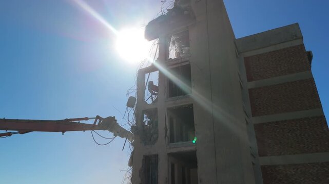 A crane demolishing a multi-story building in sunny weather.