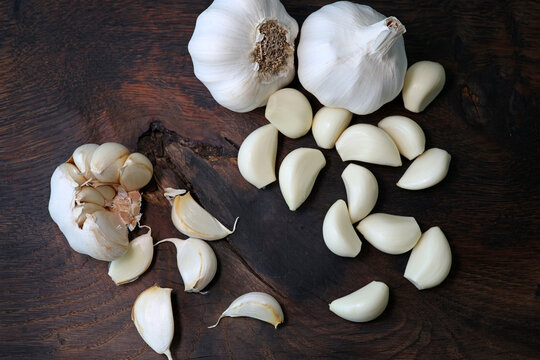 Garlic cloves in a bowl with peeled garlic on wooden background