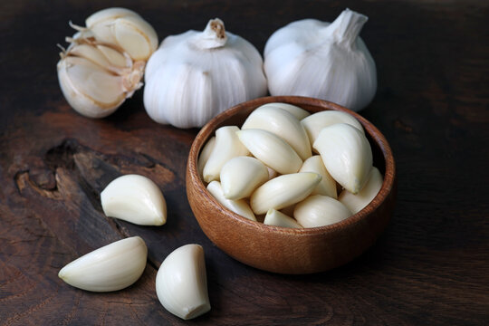 Garlic cloves in a bowl with peeled garlic on wooden background