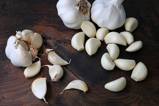 Garlic cloves in a bowl with peeled garlic on wooden background