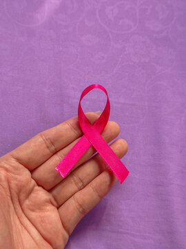 Pink awareness ribbon held in hand against a purple background, symbolizing breast cancer support, solidarity, and medical hope. Breast Cancer Awareness Day on October 13th