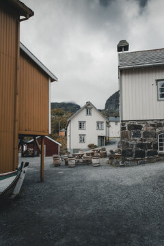 Nusfjord, Nordland, Norway - 07 September 2022: View of the historic fishing village of Nusfjord with its traditional wooden buildings, gravel paths, and rustic outdoor seating under an overcast sky.