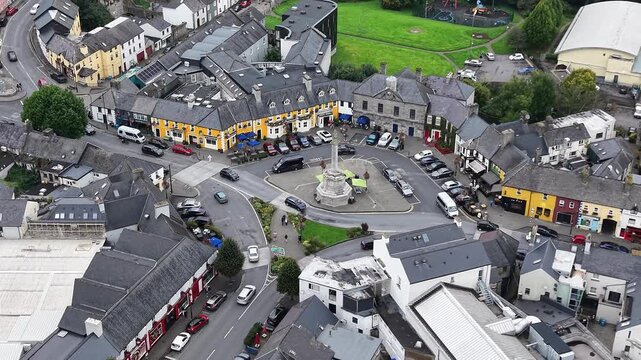 Aerial drone footage overlooking the heart of Westport, County Mayo, Ireland, featuring the historic town square, central monument, colorful traditional buildings, streets, parked vehicles and