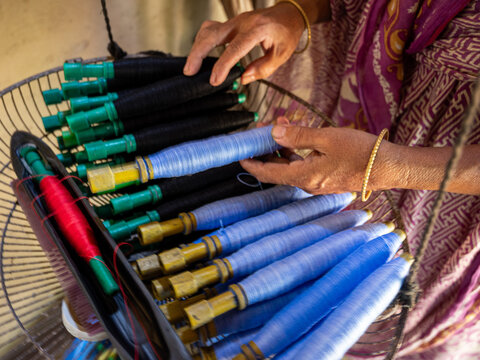 Joypurhat, Bangladesh - 22 September 2026: View of a person's hands preparing bobbins with blue and black thread for traditional textile weaving.