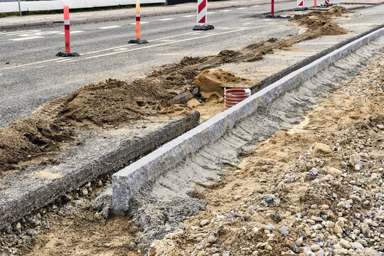 Viborg, Denmark - 07 August 2026: View of roadworks featuring the installation of new granite stone kerbs along a street with piles of sand and traffic cones.