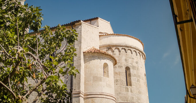 Krk, Primorje-Gorski Kotar, Croatia - 19 September 2026: View of the stone apse of a historic Romanesque church with a fig tree in the foreground under a clear blue sky.