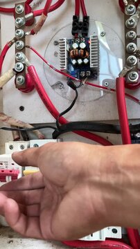 Close-up of a technician's hand switching off a miniature circuit breaker (MCB) for safety maintenance among red electrical wiring in a solar power panel box.