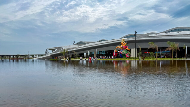 Bhogapuram, India - 22 August 2026: View of Alluri Sitarama Raju International Airport terminal building with a reflective water feature and decorative sculptures under a cloudy sky.